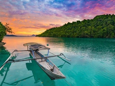 Togian Islands Indonesia sunset over caribbean sea, dramatic sky, traditional boat floating on blue green lagoon in the Togean Islands, Sulawesi, travel destination in Indonesia.