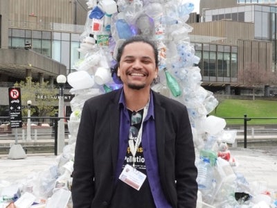Man standing in front of an art piece made of platic bottles